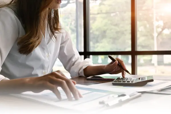 a woman sitting on desk, holding pen and calculating on calculator, seems like doing accounting